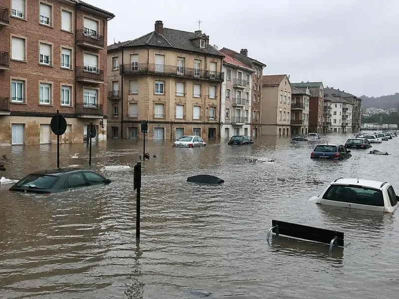 Calle urbana anegada tras lluvias torrenciales, con agua cubriendo los bajos de los edificios y vehículos parcialmente sumergidos